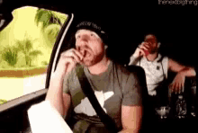 a man is smoking a cigarette in the back seat of a car while another man drinks from a red cup .