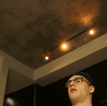 a man wearing glasses and a baseball cap is looking up at the ceiling