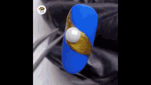 a close up of a blue and gold nail with a pearl on it