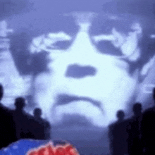 a group of people are standing in front of a projection of a man 's face on a wall .