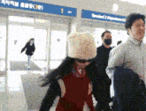 a woman wearing sunglasses and a teddy bear hat walks through an airport