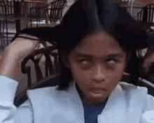 a young girl is making a funny face with her eyes closed while sitting in a chair .