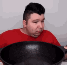 a man in a red shirt is sitting at a table eating from a wok .
