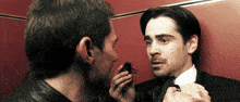 a man in a suit and tie talks to another man in a leather jacket