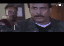 a man with a mustache is looking at the camera in a video .