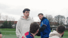a man wearing a hoodie that says lgs talks to another man on a field