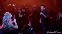 a group of people are dancing in a club and a woman is sitting at a table .