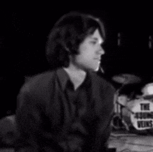 a man in a black shirt is sitting in front of a drum set in a black and white photo .