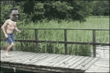 a man without a shirt is jumping off a wooden bridge into a body of water .