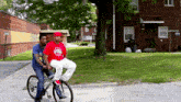 a man wearing a red shirt that says detroit sits next to another man on a bicycle