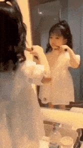 a little girl brushing her teeth in front of a mirror with a bottle of soap on the counter