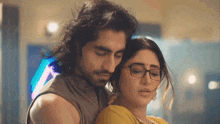 a man and a woman are hugging each other . the woman is wearing glasses and the man is without a shirt .