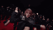 a group of people are dancing in a dark room with a woman wearing a black jacket with studs on it