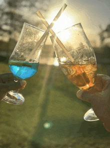 two glasses with straws in them are toasting with the sun shining through them