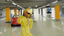 a man in a yellow suit and helmet is dancing in a parking garage with a red car in the background