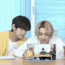 two men are sitting at a table looking at a picture of a group of people on a tablet .