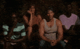 a group of people are sitting in a circle with one man wearing a tank top and a baseball cap
