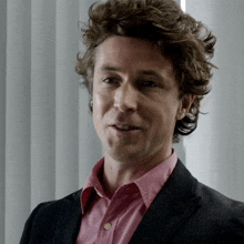 a man with curly hair and a pink shirt is smiling