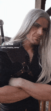 a man with long white hair and a beard is standing next to a woman with her arms crossed ..