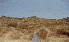 a woman in a white shirt and denim shorts stands in the desert