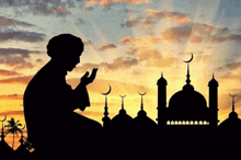 a silhouette of a person praying with a mosque in the background