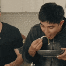 a man is eating from a bowl with a spoon and the word zky is on the bottom right