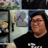 a man wearing headphones and glasses is standing in front of a wall with posters on it and a phone on it