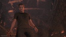 a man in a black shirt stands in front of a burning building with the words magiccalladie written below him