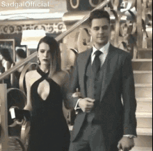 a man in a suit and tie is walking with a woman in a black dress