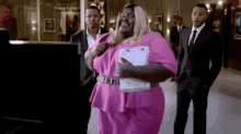 a woman in a pink dress is holding a clipboard and smiling while two men in suits stand behind her .