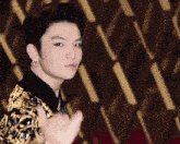 a young man wearing a gold and black jacket and earrings looks at the camera