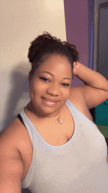 a woman wearing a tank top and a necklace smiles for a picture