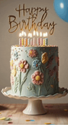 a birthday cake with flowers on it is on a cake stand with candles .