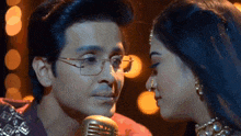 a man and woman are kissing in front of a microphone . the man is wearing glasses .