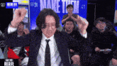 a man in a suit and tie is dancing in front of a make them believe sign
