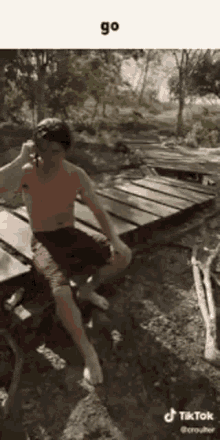 a shirtless man is sitting on a wooden bench holding a stick .