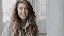 a woman with long hair and a denim jacket is smiling in a room .