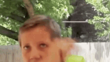a young boy is holding a tennis ball in front of a fence and looking at the camera .
