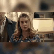 a woman is standing in front of a lamp in a room with a man behind her