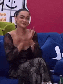 a woman in a black dress is sitting on a blue couch applauding .