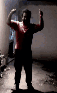 a man in a red shirt is standing in the dark with his arms in the air
