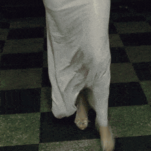 a woman in a white dress is walking on a green and black checkered floor