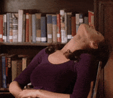 a woman in a purple shirt is sitting in front of a bookshelf with a book called allan