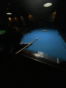 a woman is playing pool in a dark room with a blue cloth