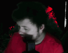 a man in a red shirt is talking into a microphone in a dark room