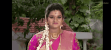 a woman in a pink saree and gold jewelry is standing in front of a house .