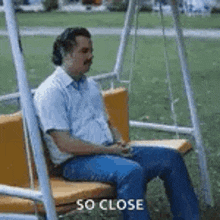 a man is sitting on a swing with the words `` so close '' written below him .