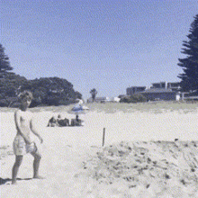 a man standing on a sandy beach with a few people sitting on the beach