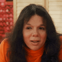 a woman with long dark hair and a nose ring looks at the camera