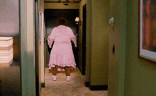 a woman in a pink robe is walking down a hallway .